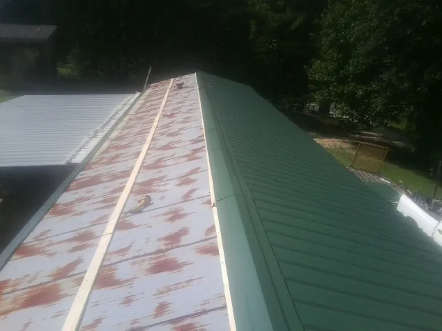 Old rusted panels beside newly installed green metal roofing — Wind Damage Roof Repair by Roofing Brothers in Heathsville