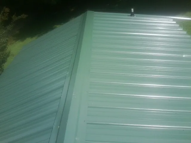 New green metal panels meeting at the ridge of a roof — Flat Roof Repair work by our crew in Heathsville