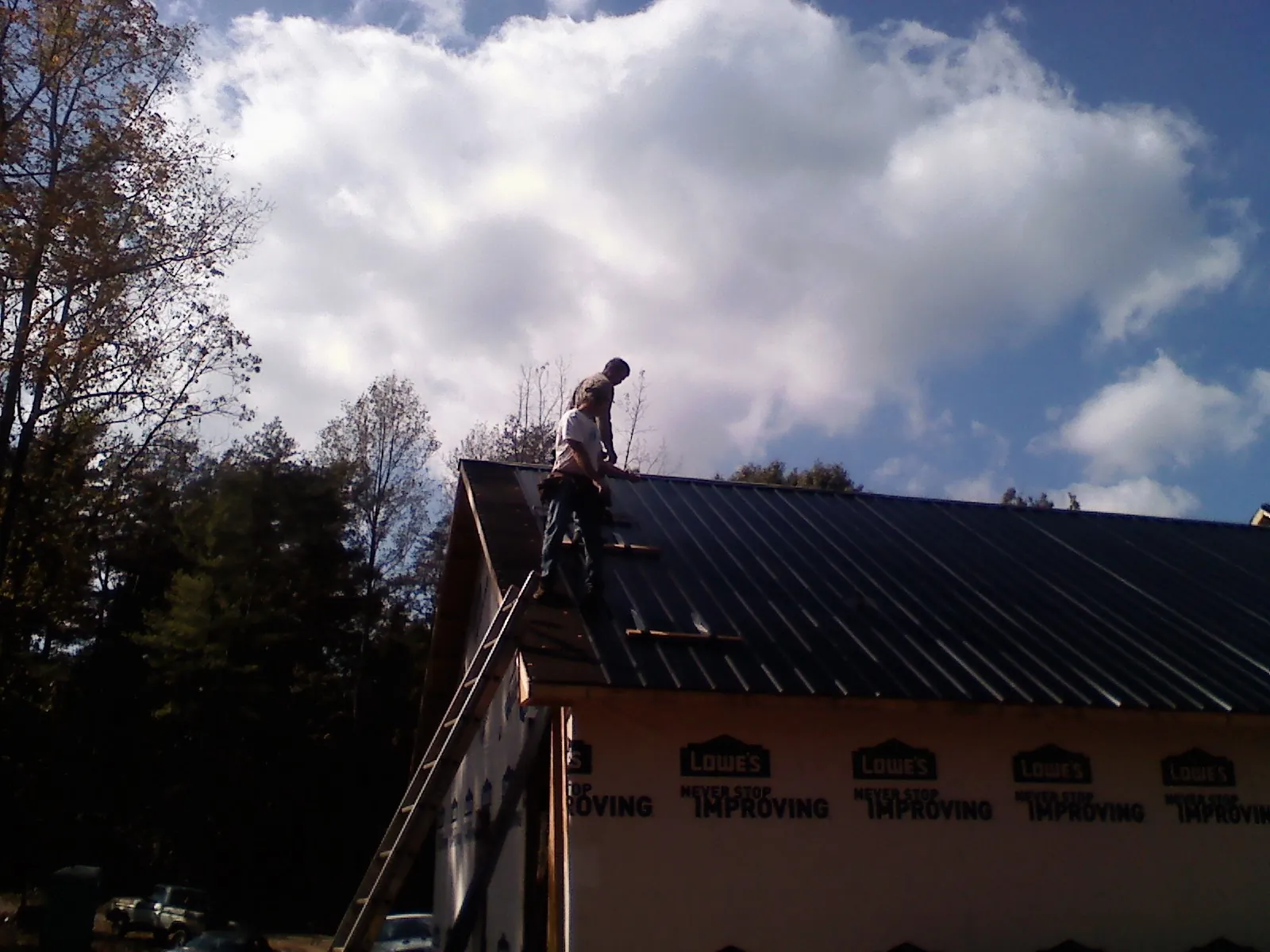 Roofer fastening dark metal panels high against a cloudy sky, from a Roof Inspection job in Heathsville