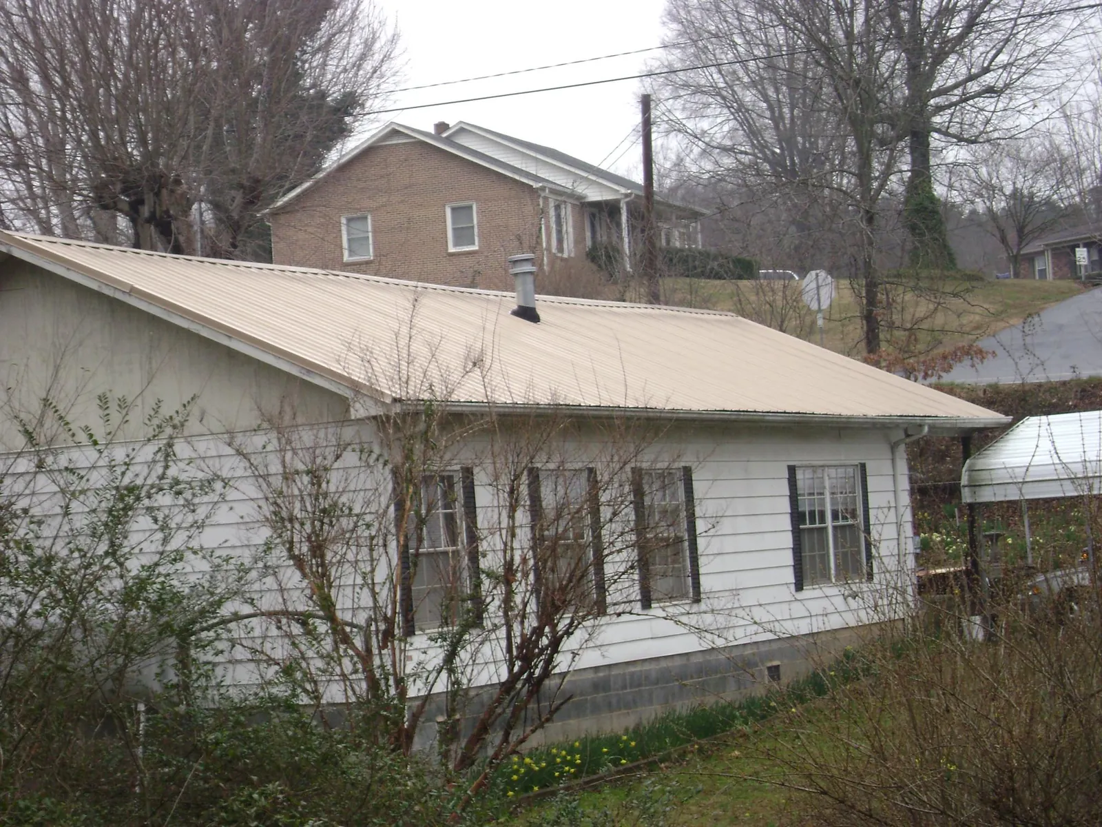 Tan metal roof on a white sided house set into a hillside — Commercial Roofing by Roofing Brothers in Heathsville
